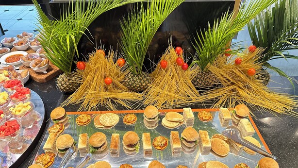 A buffet with various food items including sandwiches, burgers, and pasta, arranged on a table with decorative plants and pineapples. - Golden Tulip Hotel PH-GTPH (Port Harcourt)