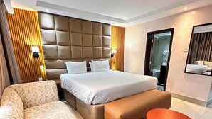 A modern hotel room with a large bed, a sofa, a small round table, and a mirror. - Golden Tulip Hotel PH-GTPH (Port Harcourt)