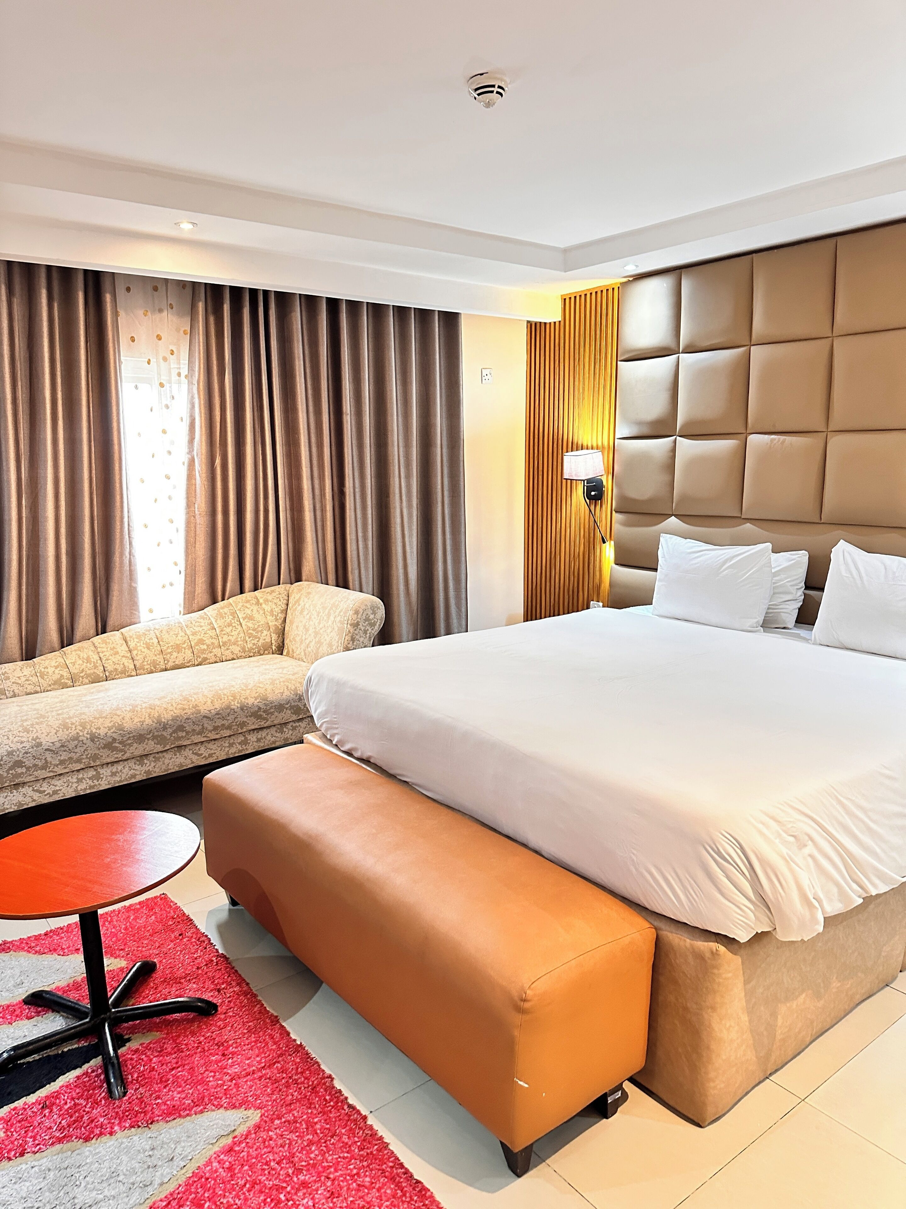 A hotel room with a large bed, a sofa, a small table, and a bench.