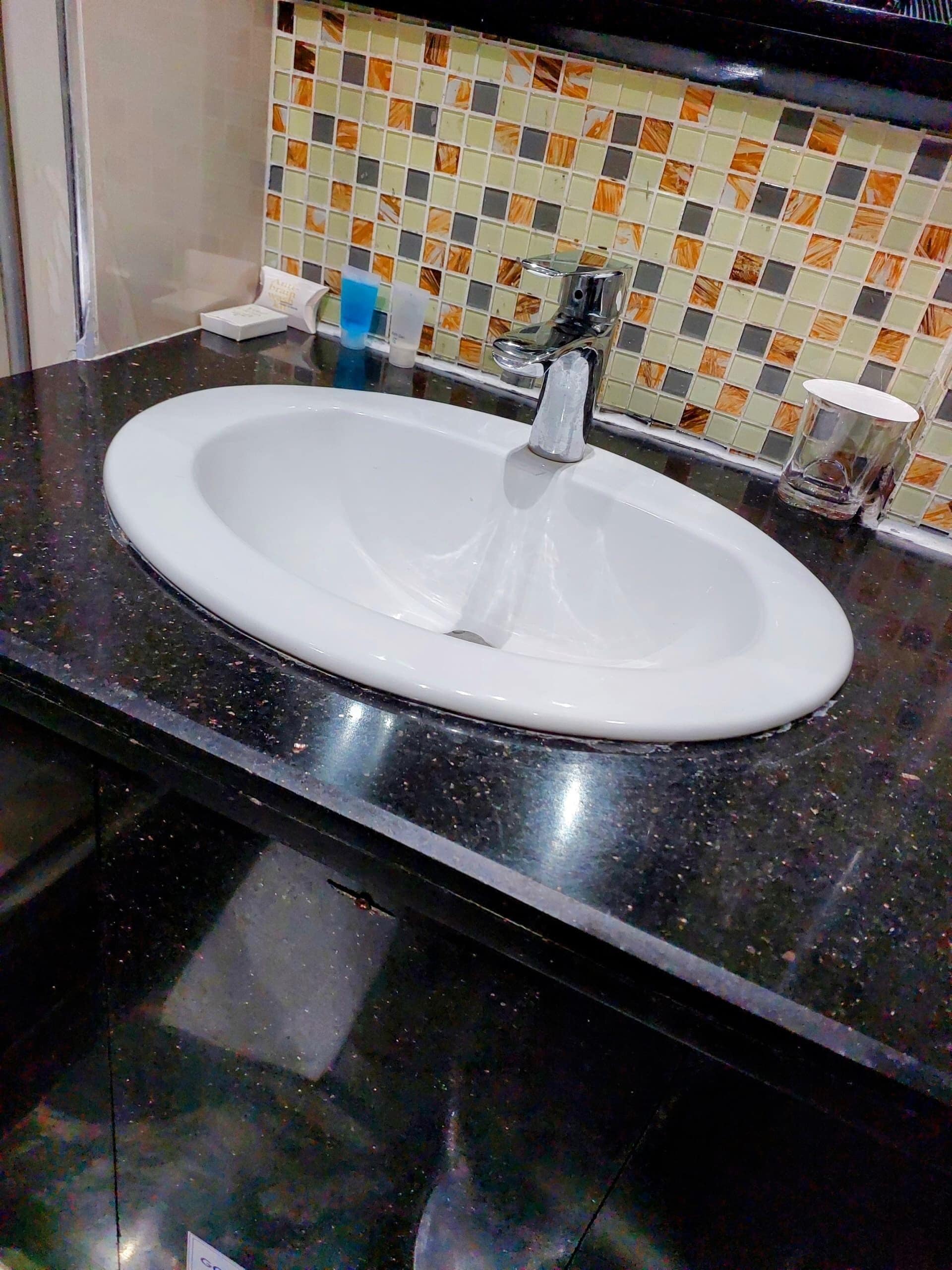 A bathroom sink with a modern faucet, a tiled backsplash, and a dark countertop.