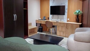 A modern living room with a sofa, a coffee table, a TV, and a wooden desk with a chair. - Golden Tulip Hotel PH-GTPH (Port Harcourt)