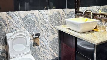 Un baño con pared de mármol, un lavabo blanco y un inodoro.