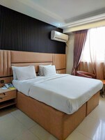 A hotel room with a large bed, a bedside table with a phone, a chair, and a window with curtains.