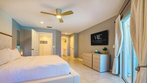 A modern bedroom with a large bed, a ceiling fan, a wall-mounted TV, and a window with curtains.