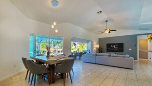 A spacious living area with a dining table, gray sofa, and a TV displaying 'Vacation Rentals Cape Coral'.