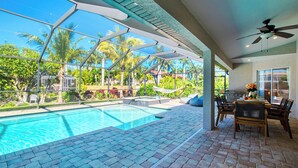 A pool area with a view of palm trees and a dining area with chairs and a table.