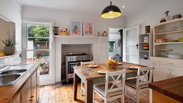 A kitchen with a wooden table, white chairs, a gas stove, and a hanging light fixture.