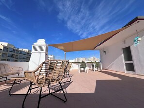 A rooftop terrace with wicker chairs, a table, and a large umbrella providing shade.