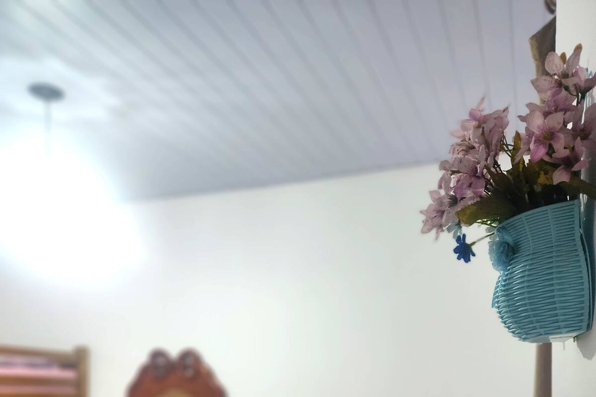 A bedroom with a bunk bed, a wooden chair, a bedside table, and a wall-mounted shelf with flowers.
