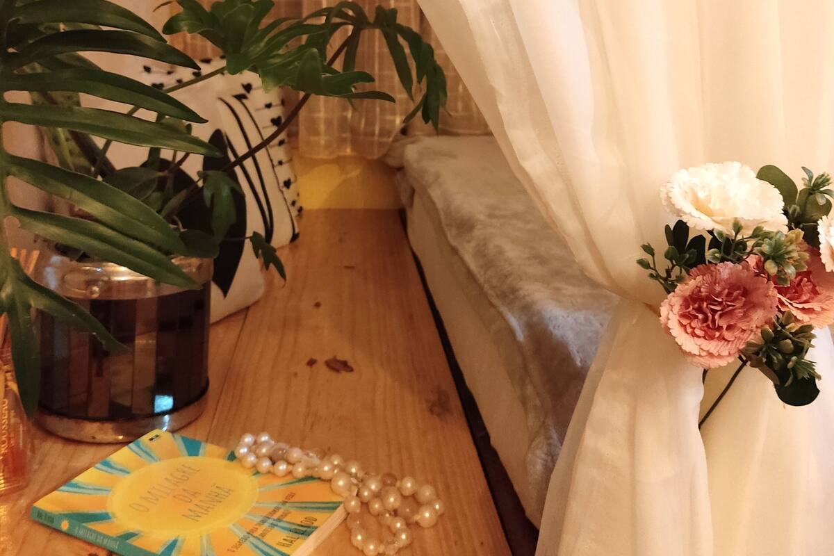 A wooden bedside table with a book, a candle, and a string of pearls.