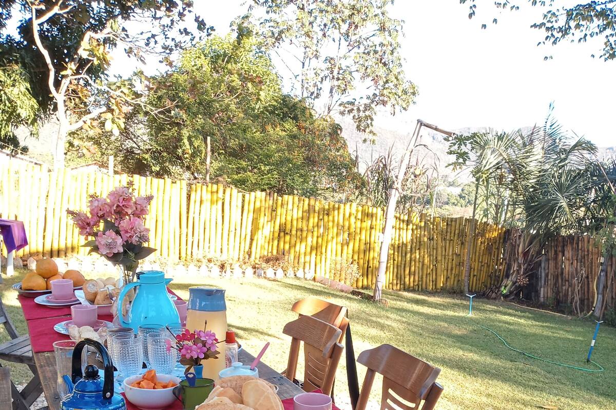 A picnic setup with a table covered in a red tablecloth, featuring various food items, cups, and a pink water jug.