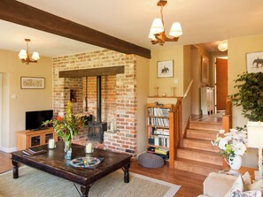 A living room with a brick fireplace, wooden bookshelves, a coffee table with a board game, a television, and a staircase leading to another level.