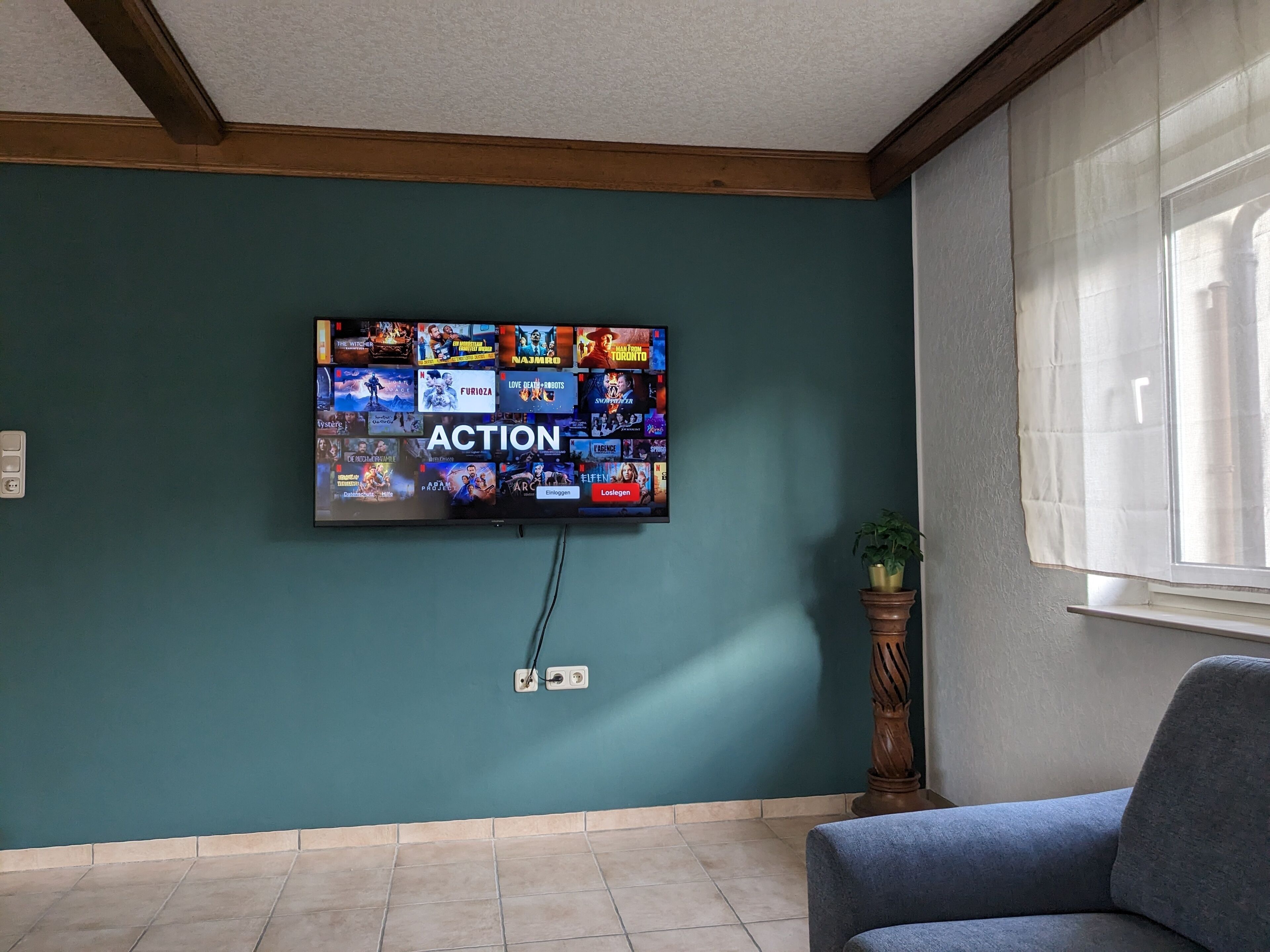 Una sala de estar con un televisor de pantalla plana montado en una pared color turquesa que muestra diferentes servicios de streaming.
