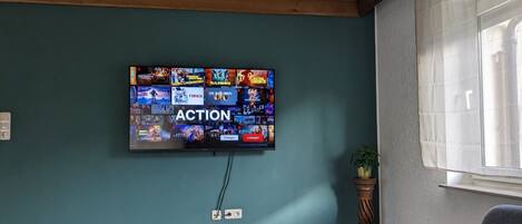 Una sala de estar con un televisor de pantalla plana montado en una pared color turquesa que muestra diferentes servicios de streaming.