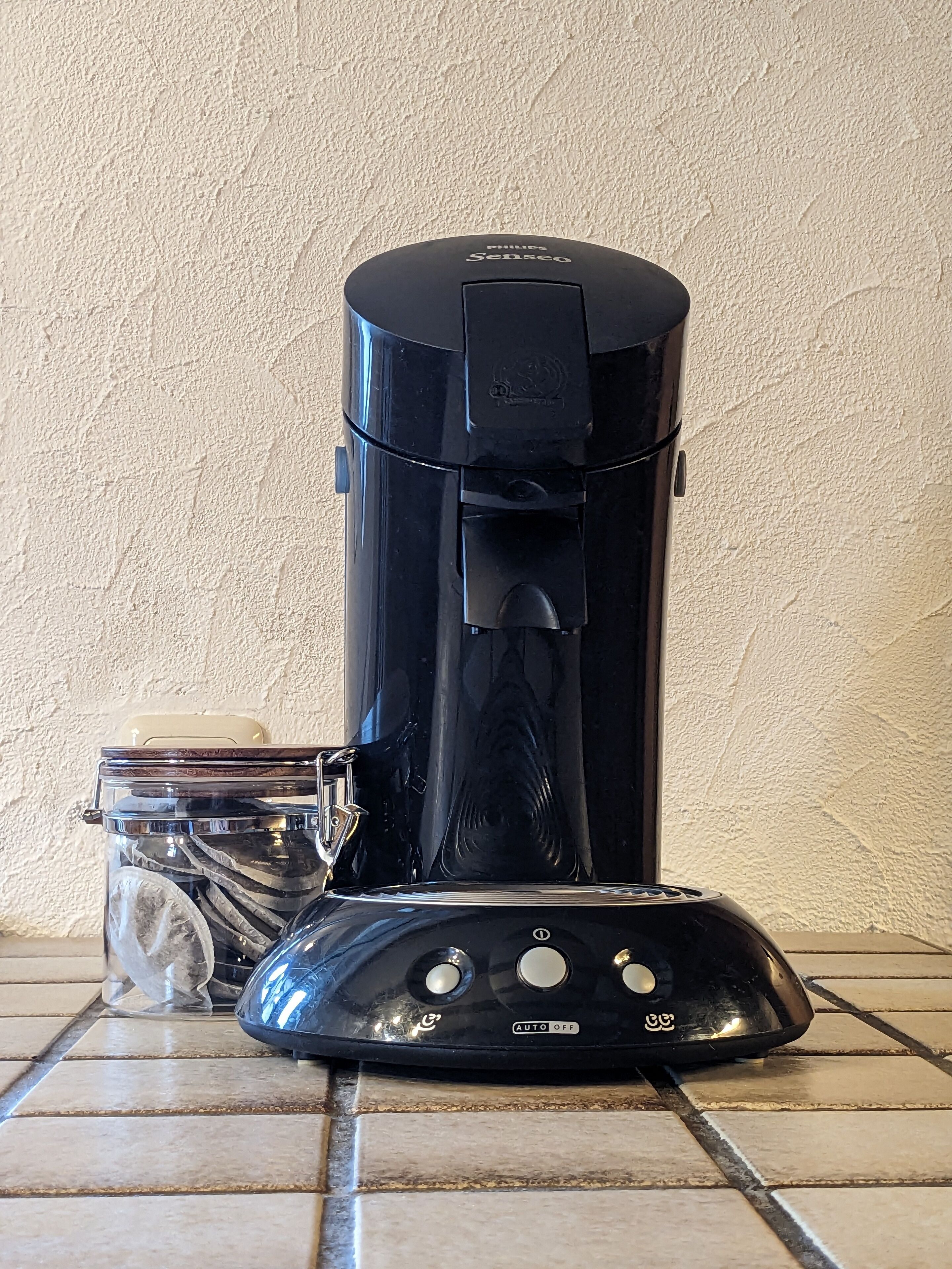 A black coffee maker with a clear water reservoir and a glass carafe on a tiled surface.