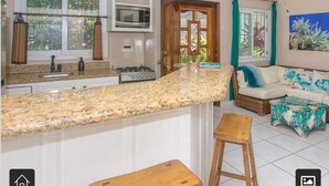 Een keuken met granieten aanrecht, een magnetron en een fornuis. Er staat een houten kruk en een rieten bank met een blauw kussen.