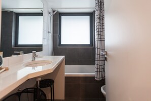 A modern bathroom with a large window, a bathtub, and a toilet.
