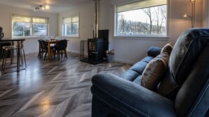 A modern living room with a fireplace, dining area, and large windows. - Rivendell House located close to Fort William (Spean Bridge)