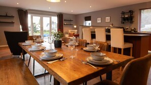 A dining area with a long wooden table set for a meal, surrounded by chairs. - Cairn Cottage in the village of Onich (Onich)