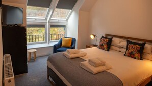 A bedroom with a large bed, a chair, a TV, and a window with a balcony view. - Cairn Cottage in the village of Onich (Onich)