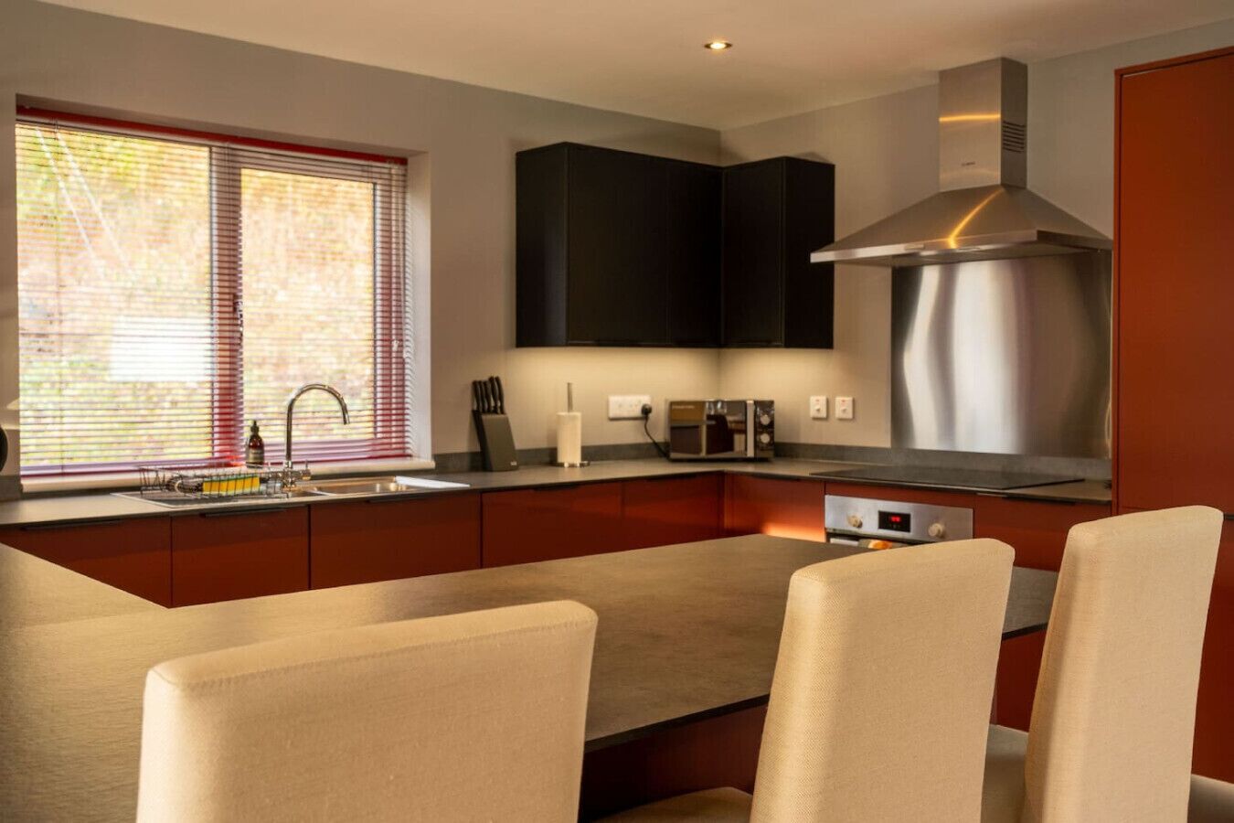 A modern kitchen with dark cabinets, a stainless steel range hood, and a built-in oven.