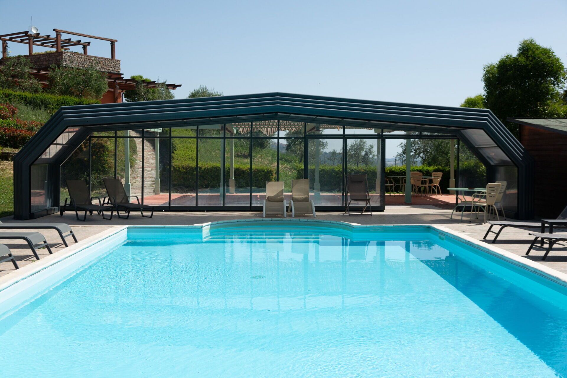 Ein Schwimmbecken mit Glasveranda, Liegestühlen und einer Terrassenanlage mit Tischen und Stühlen.