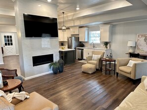 A spacious living room with a fireplace, a dining area, and a kitchen in the background. - Elegant 3 BR House, Fenced Yard, Crews, Couple, Relaxing Getaway (Tyler)