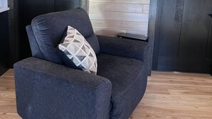A modern living room with a dark blue sofa, a patterned cushion, and a wooden floor.