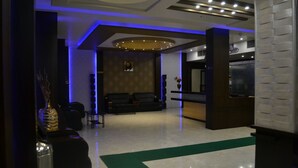 A modern lobby with a reception desk, seating area, and a large TV screen. - The Grand Rajwada (Seoni)