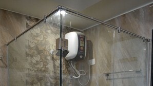 A glass-enclosed shower stall with a handheld showerhead, a hand dryer, and a small trash bin. - The Grand Rajwada (Seoni)