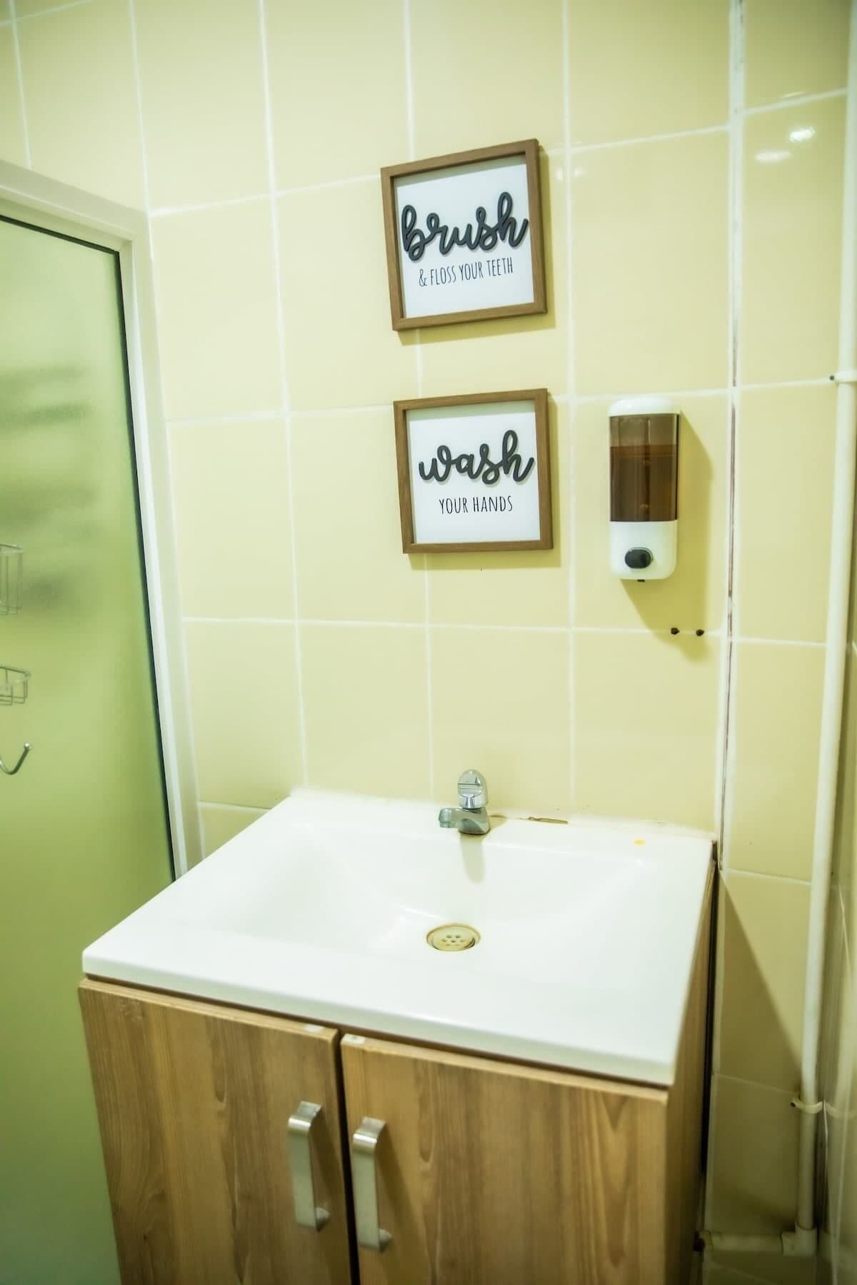 Un baño con un lavamanos blanco, armarios de madera y dos carteles enmarcados en la pared.