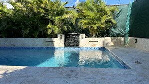 A swimming pool with a tiled edge, surrounded by a stone deck and palm trees.