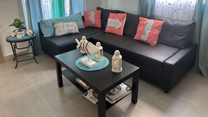 A living room with a black leather sofa, teal and coral cushions, a small side table with a plant, and decorative items.
