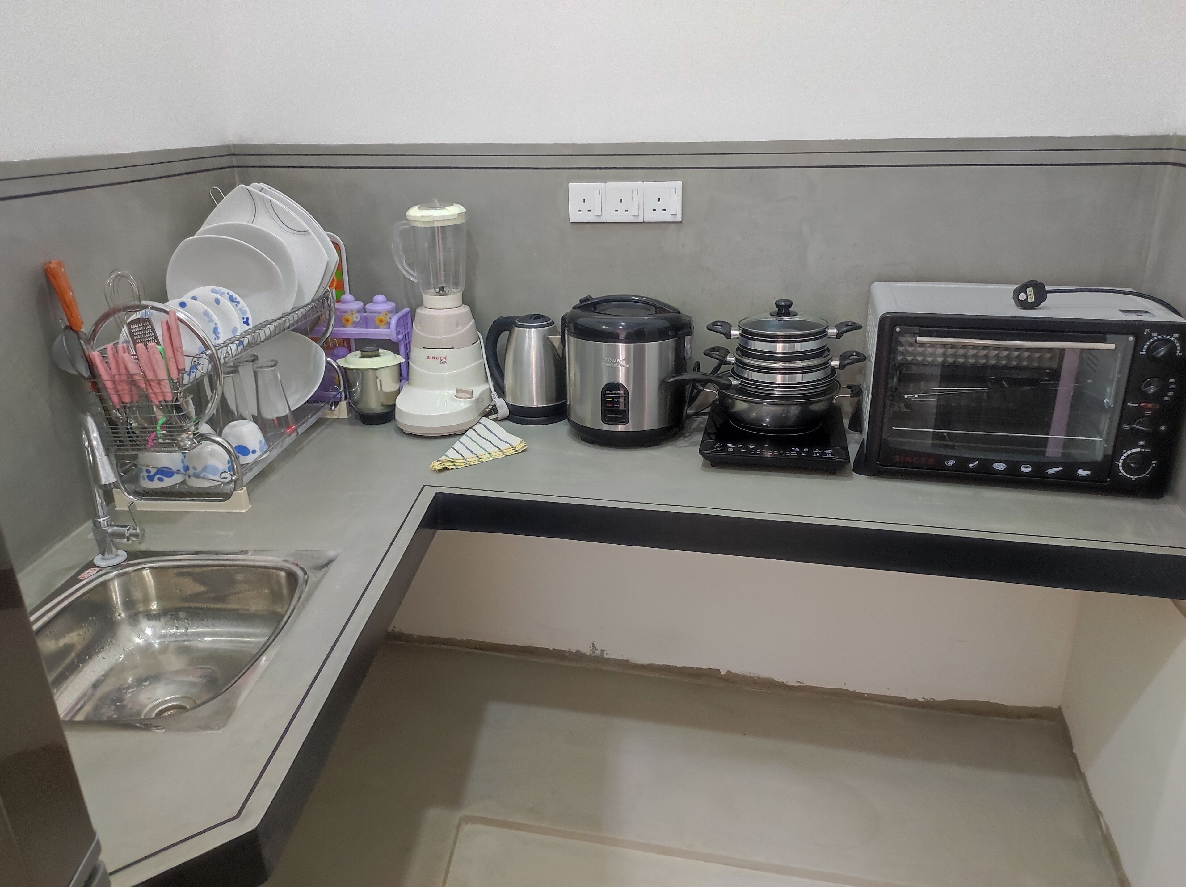 A compact kitchen with a sink, a dish rack, a blender, a kettle, a coffee maker, a rice cooker, and a toaster oven.