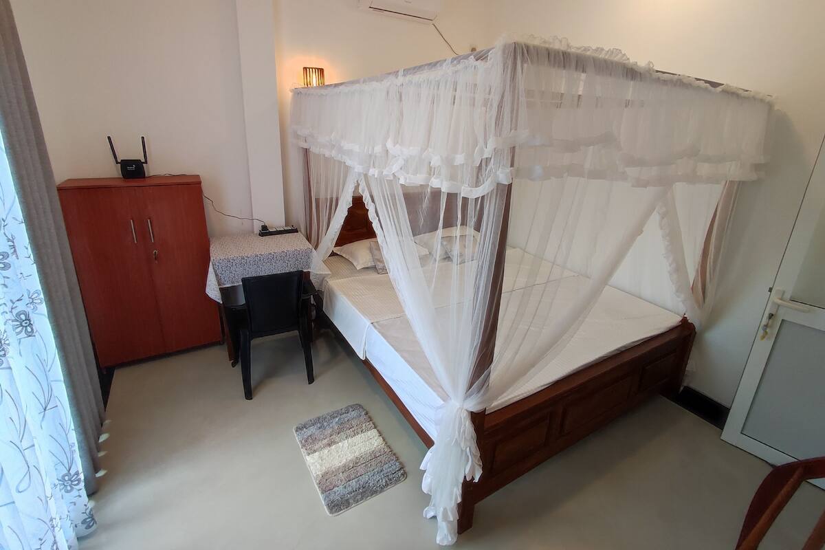 Un dormitorio con cama de madera, una mesita de noche, un escritorio, un armario y un mosquitero.