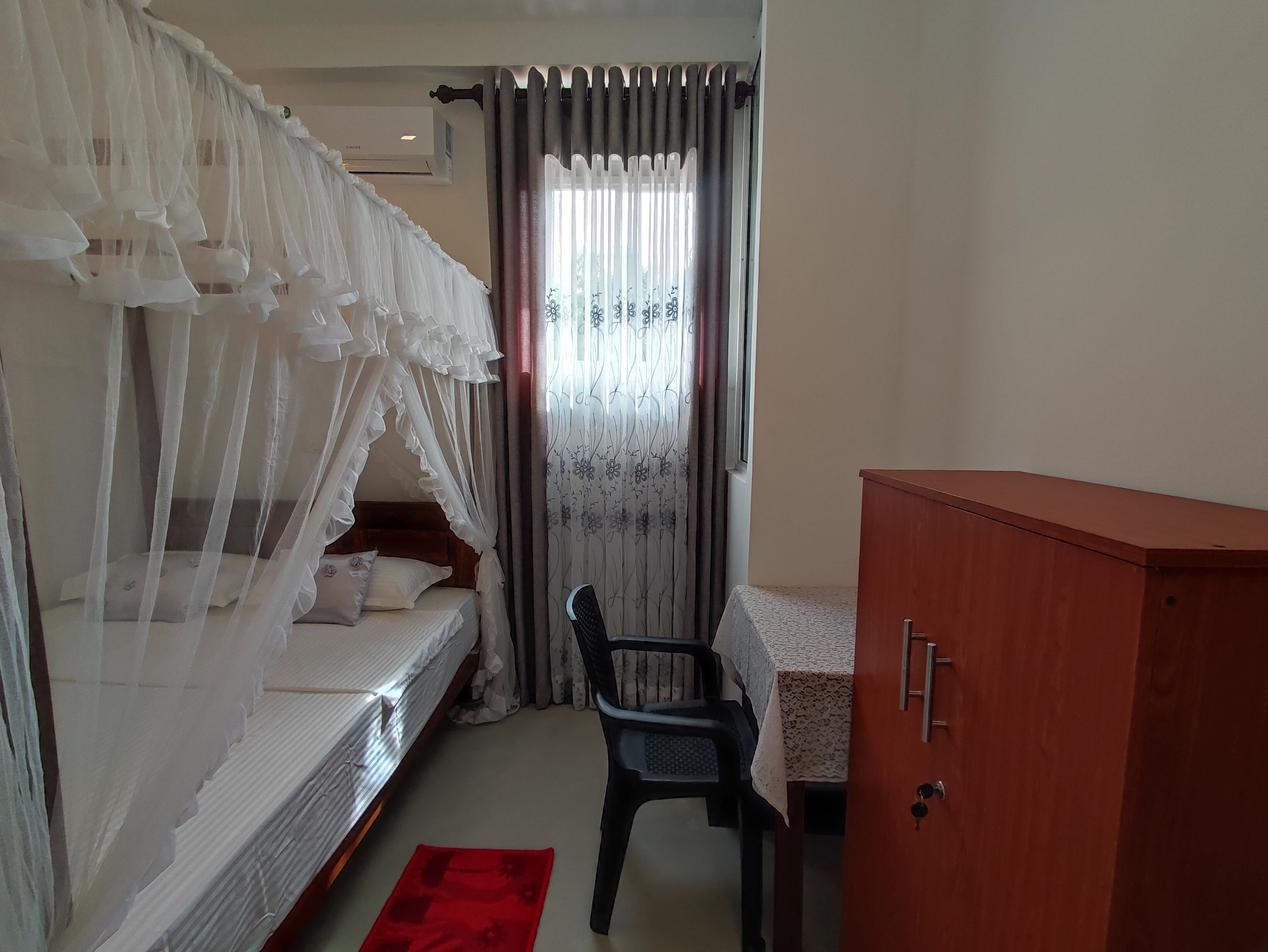 A bedroom with a bed, a chair, a wardrobe, and a window with curtains.