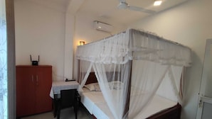 A bedroom with a bed under a canopy, a desk with a chair, a wardrobe, and a ceiling fan. - Flower shade villa (Weligama)