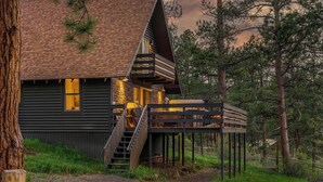 A cabin with a wooden exterior, a balcony, and a staircase leading to the upper level. - Elegant A-Frame w/ Hot Tub Views! Close to town, skiing, & hiking! (Evergreen)