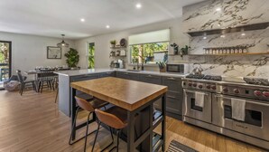 A modern kitchen with a marble backsplash, stainless steel appliances, and a wooden dining table. - Elegant A-Frame w/ Hot Tub Views! Close to town, skiing, & hiking! (Evergreen)