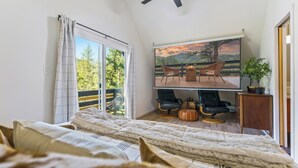 A bedroom with a large bed, a ceiling fan, a TV on the wall, and a balcony with outdoor furniture. - Elegant A-Frame w/ Hot Tub Views! Close to town, skiing, & hiking! (Evergreen)