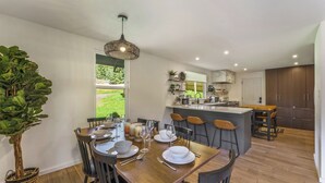 A modern kitchen with a dining area, wooden flooring, and a large potted plant. - Elegant A-Frame w/ Hot Tub Views! Close to town, skiing, & hiking! (Evergreen)