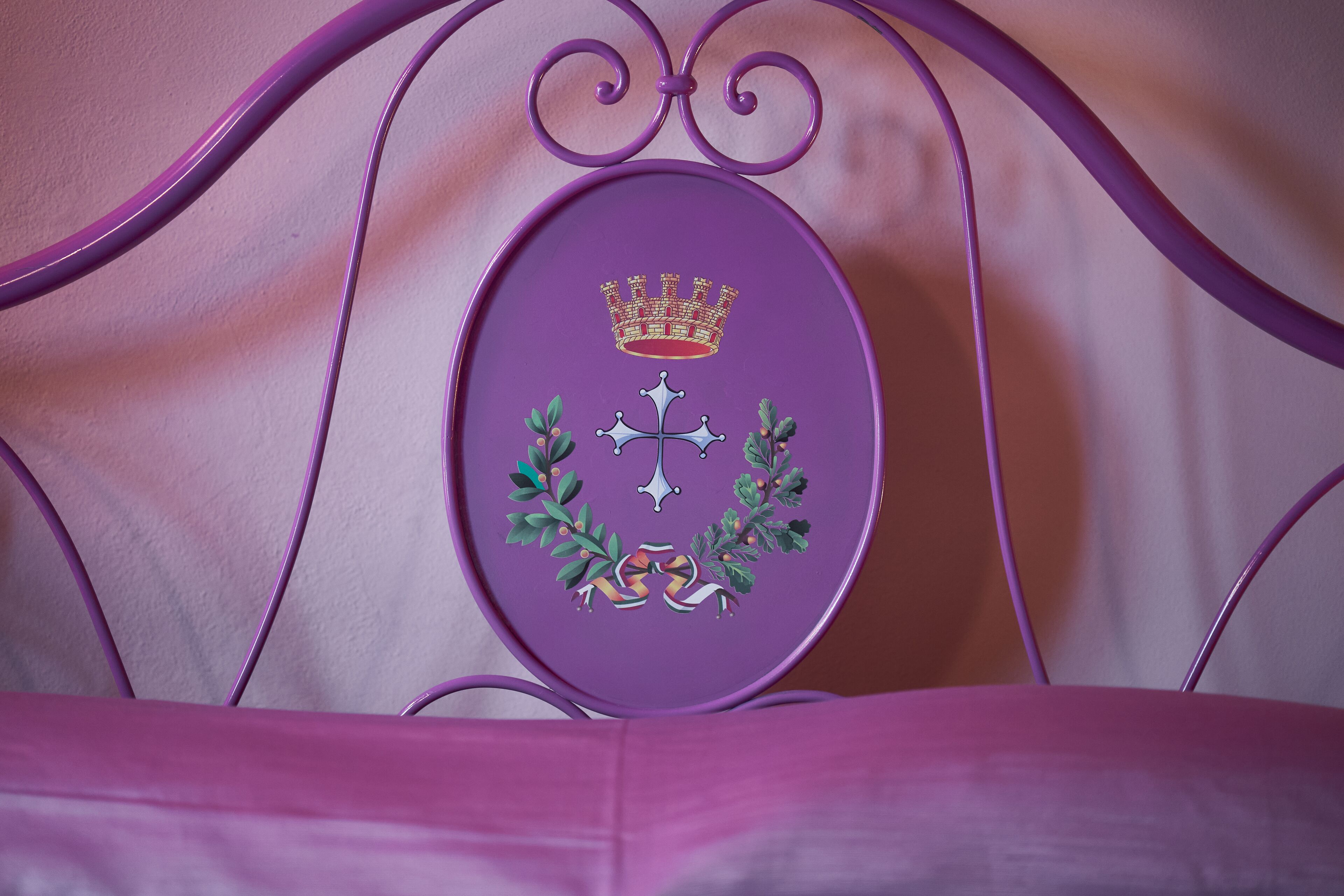 A purple metal bed frame with a decorative emblem featuring a crown, cross, and laurel wreath.