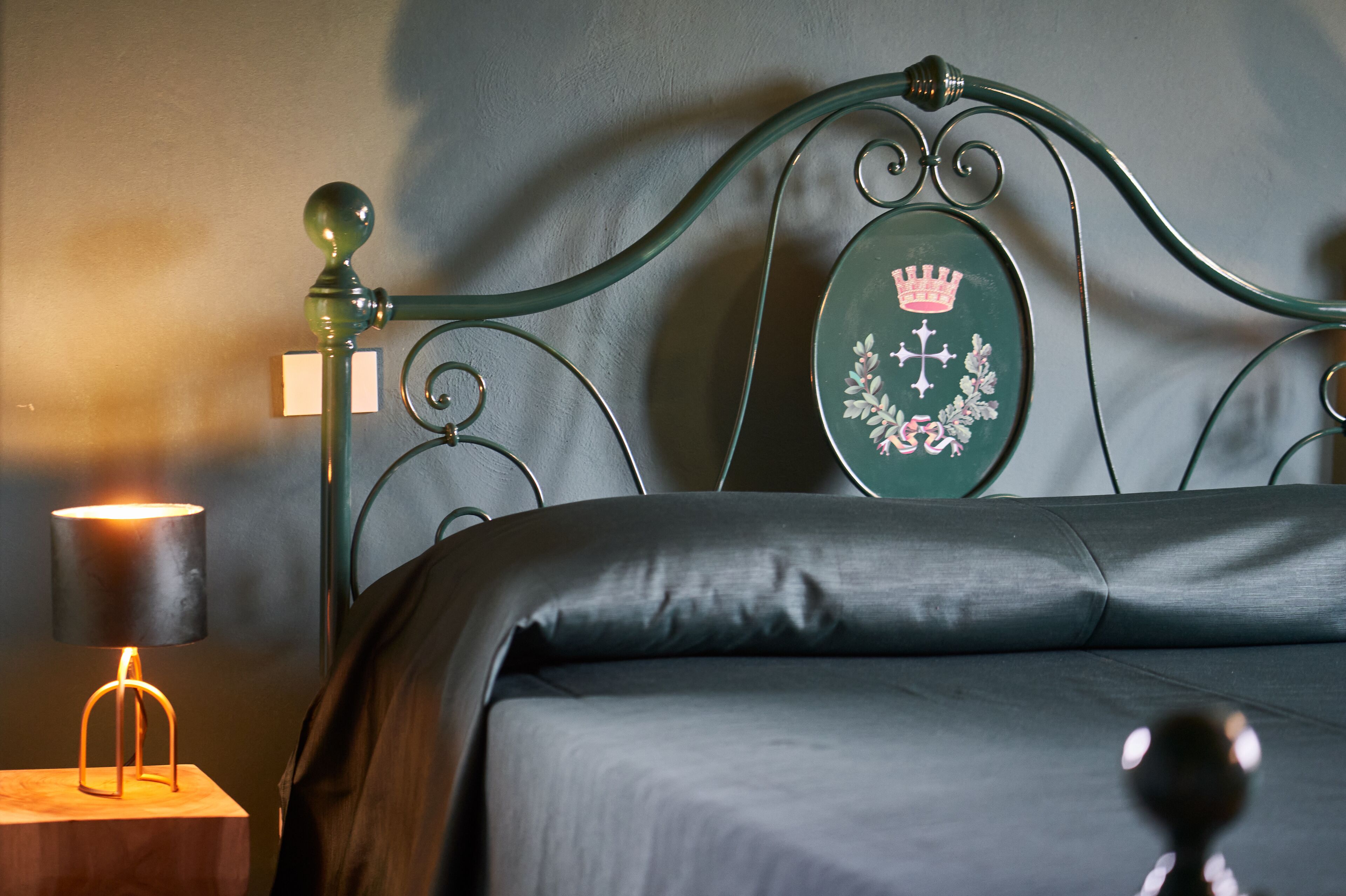 Een bed met een groen hoofdeinde, een bedlamp en een klein tafeltje met een lamp.