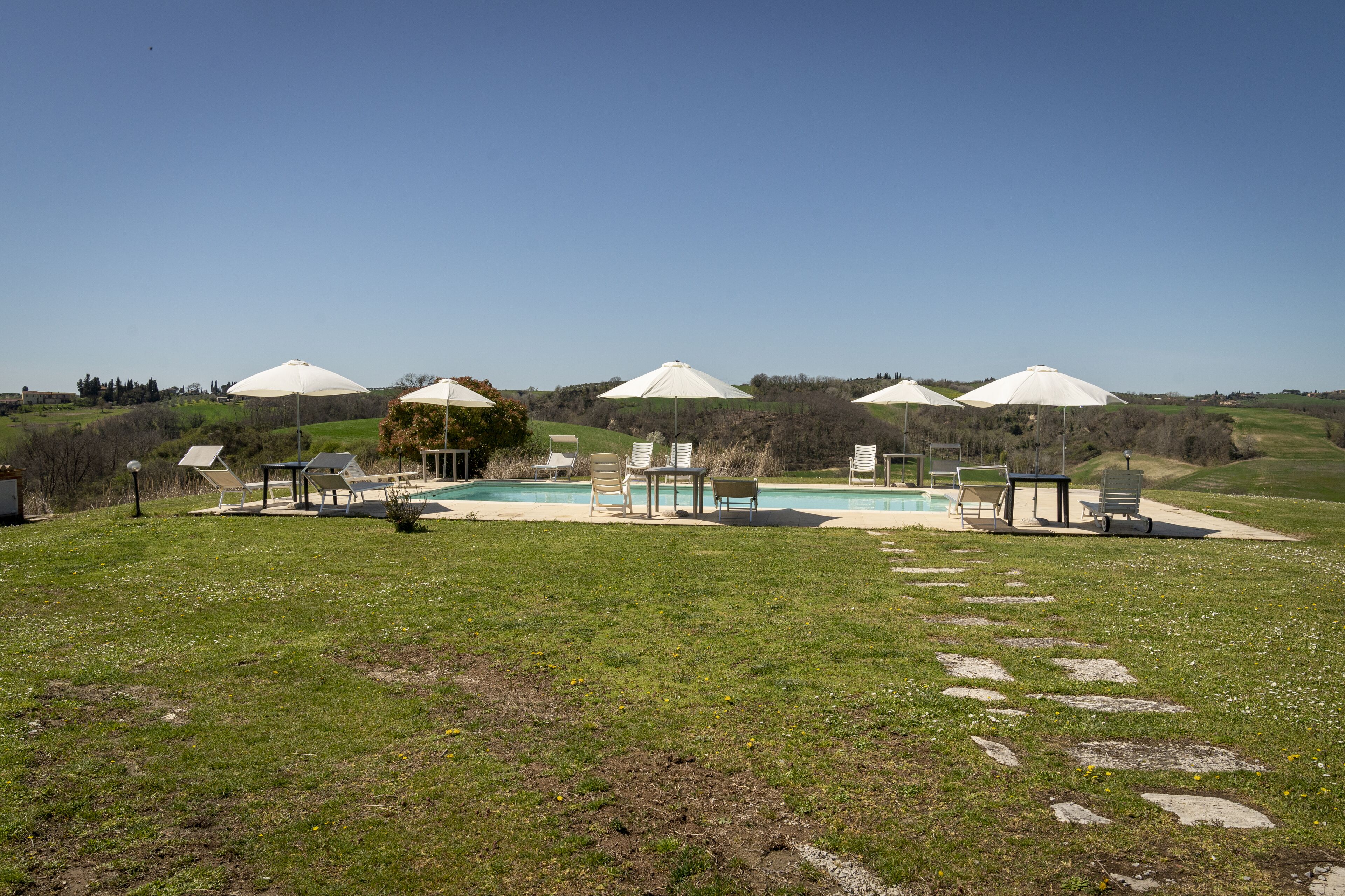 Zona de piscina con sombrillas, sillas de descanso y cielo despejado.