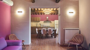 A modern kitchen with a dining area, wooden ceiling beams, and a pink wall. - Podere Sant'Antonio (Asciano)
