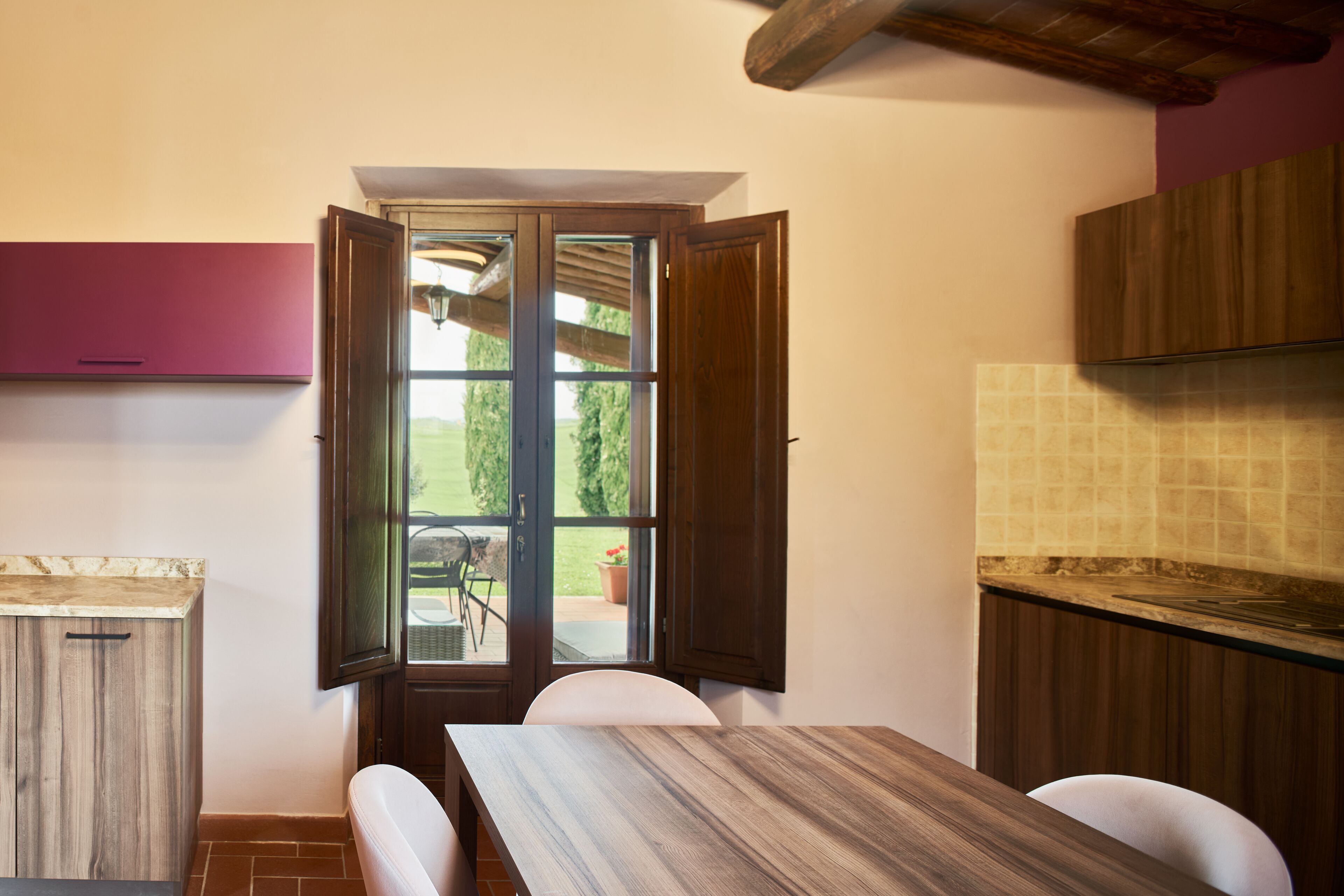 Una cocina con una mesa y sillas de madera, una ventana con persianas abiertas y vistas al exterior.
