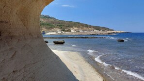 Een kustlandschap met een helder uitzicht op de zee, een zandstrand en rotsformaties.