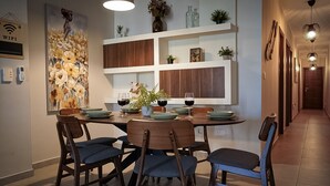 Un comedor con una mesa redonda, sillas y un estante en la pared con objetos decorativos.