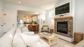 A modern living room with a stone fireplace, a sofa, a coffee table, and a dining area in the background.