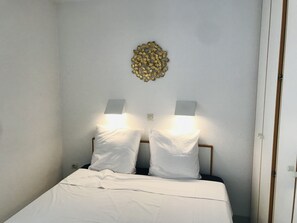 A bed with white bedding and two wall-mounted lamps. - Costa Plana Collection (Cap d'Ail)